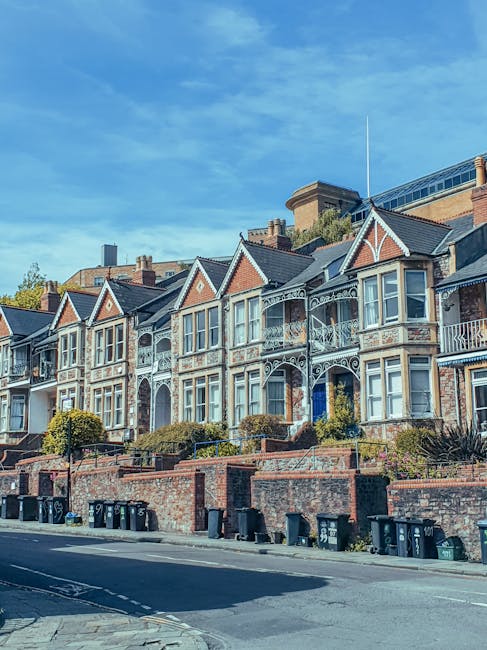 The image shows the upper section of a multi-storey residential building with a brick facade and white window frames. Two windows on the second floor have flower boxes with plants and flowers, one of